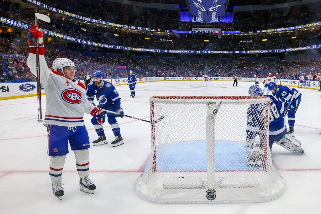 Cole Caufield raises his arm in the air as he skates by the Tampa net, in a photo shot from behind the net