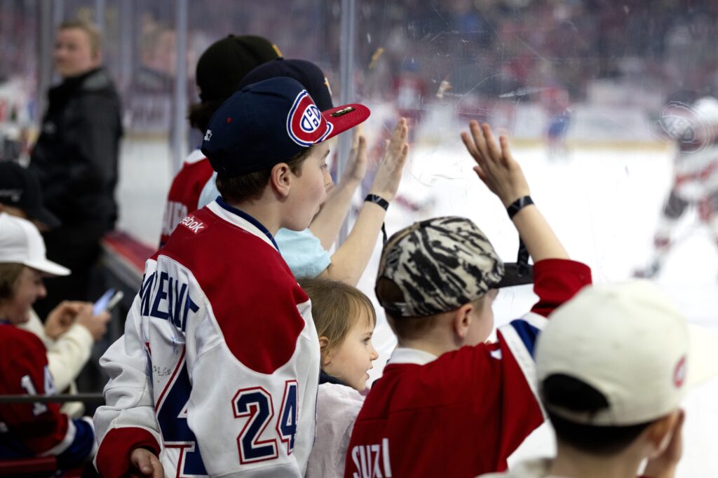 Children in Canadiens jerseys watch players on the ice from seats just behind the glass.