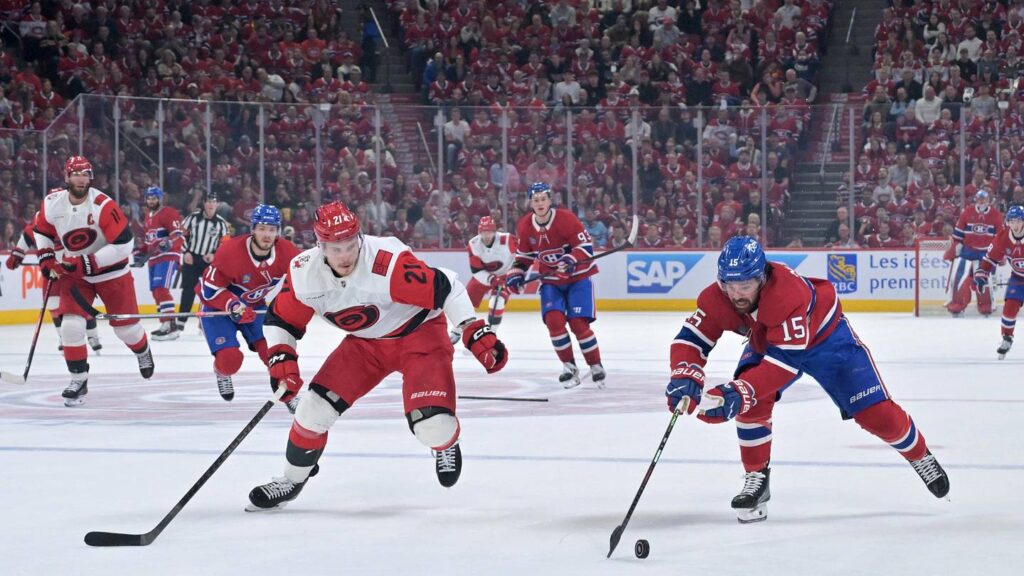 May 25, 2026; Montreal, Quebec, CAN; Montreal Canadiens center Alex Newhook (15) reaches for a puck against Carolina Hurricanes defenseman Alexander Nikishin (21) during the first period in game three of the Eastern Conference Final of the 2026 Stanley Cup Playoffs at Bell Centre. Mandatory Credit: Eric Bolte-Imagn Images