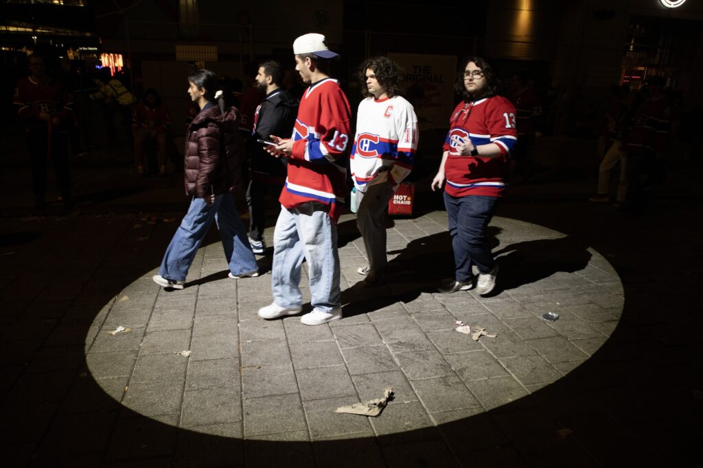 Five Canadiens fans walk through an illuminated circle of pavement at night.