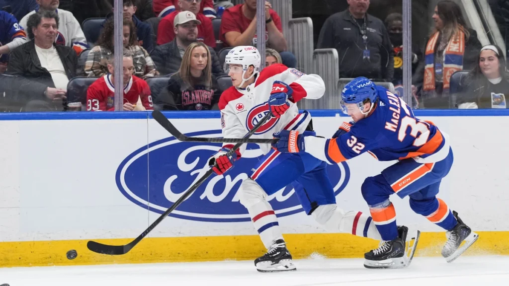 Montr&eacute;al Canadiens defenseman David Reinbacher (64) passes the puck as New York Islanders center Kyle MacLean (32) chases in the second period at UBS Arena.