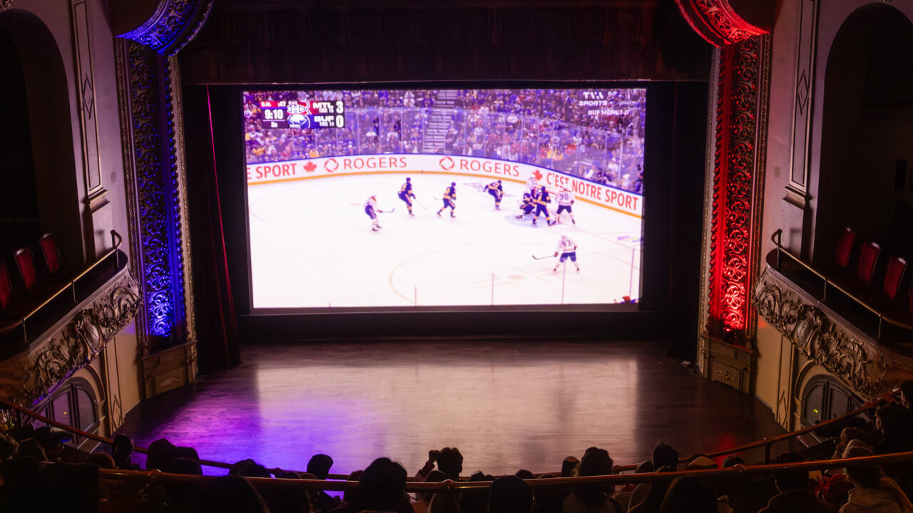 People sitting in movie theatre watching hockey game on big screen.