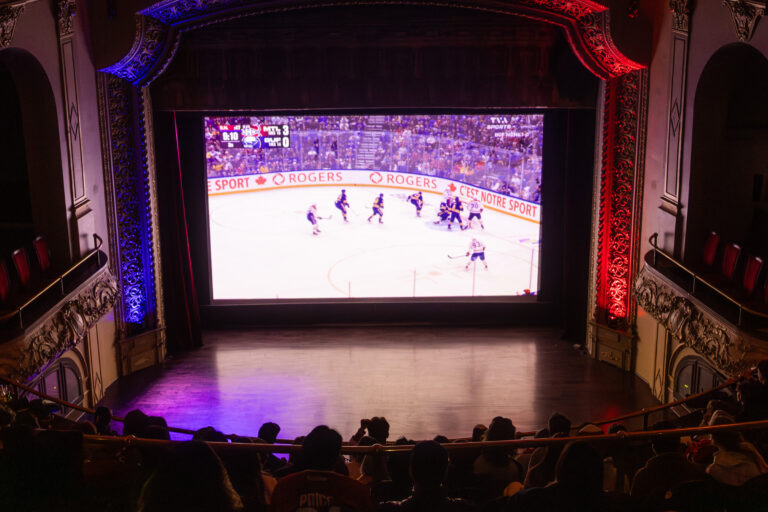 People sitting in movie theatre watching hockey game on big screen.