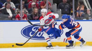 Apr 12, 2026; Elmont, New York, USA; Montréal Canadiens defenseman David Reinbacher (64) passes the puck as New York Islanders center Kyle MacLean (32) chases in the second period at UBS Arena. Mandatory Credit: Alexander Wohl-Imagn Images
