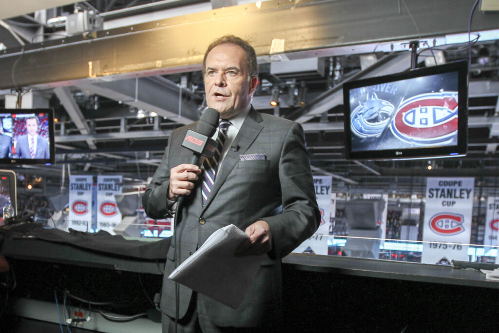 RDS hockey play-by-play announcer Pierre Houde stands in media area at Bell Centre with an RDS microphone in his hand and monitors behind him.