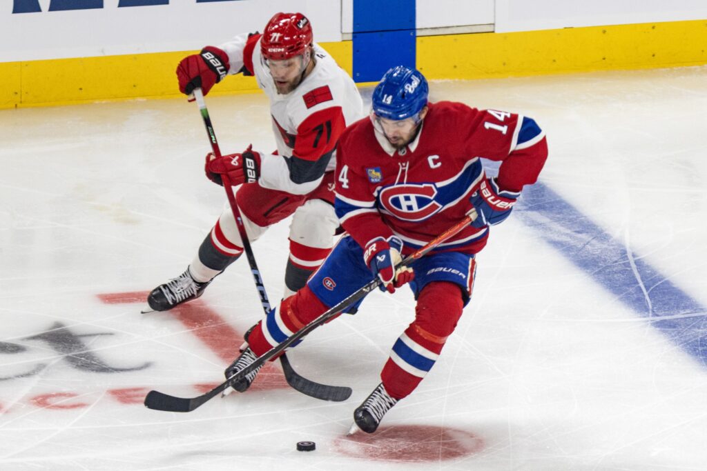 Canadiens captain Nick Suzuki protects the puck from the checking of Hurricanes' Taylor Hall.